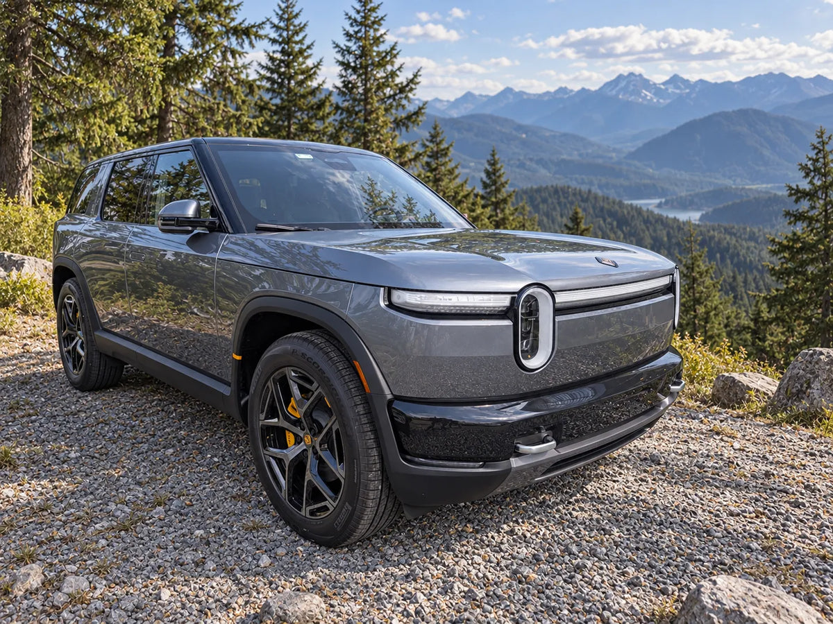 Gray Rivian R2 parked at a forest overlook with mountains in the distance